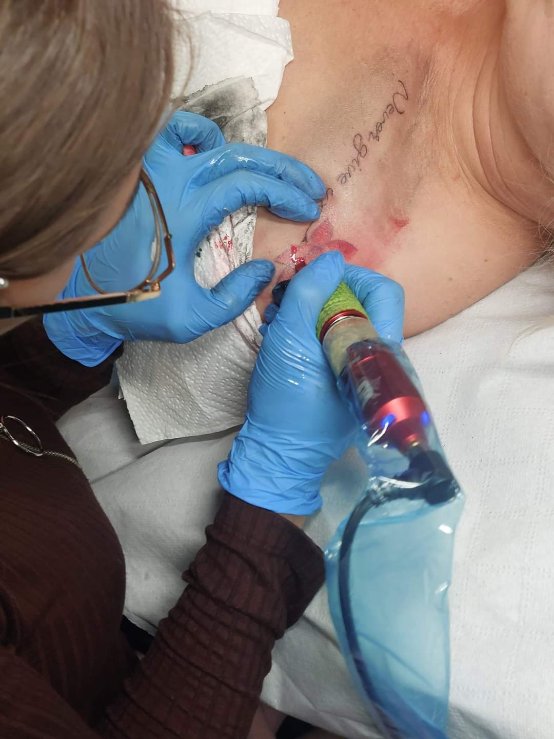 Tatuażystka pracująca w niebieskich rękawicach na sterylnym białym podłożu - Omnia Studio Tattoo, Łask