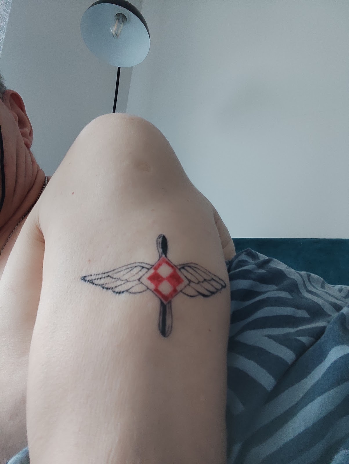 Tatuaż na ramieniu - skrzydła z lotniczym symbolem w czerwieni